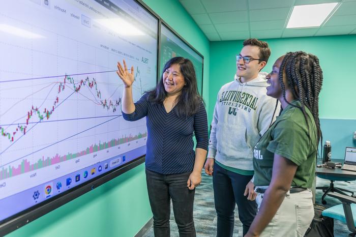 Professor and students use financial forecasting tool on projection screen.