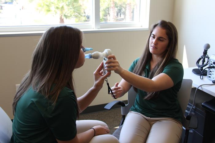 Two students practicing speech therapy techniques with equipment.