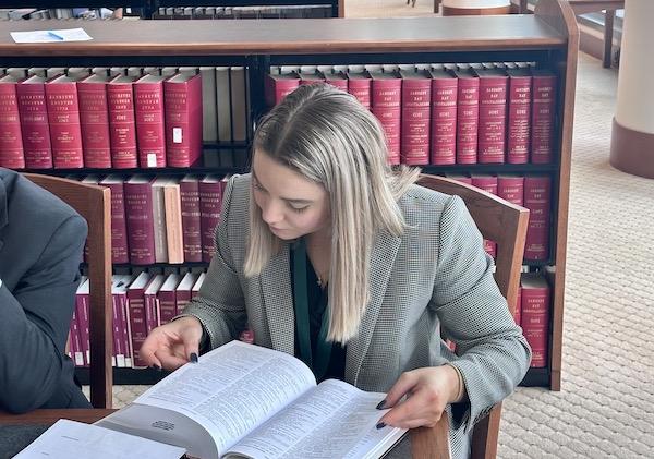 A female student reading a textbook at a table in a courthouse library.