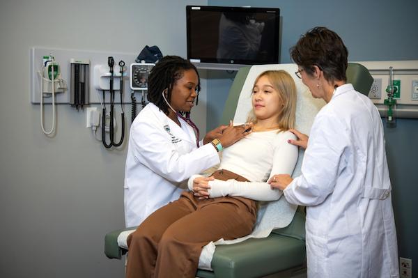 A nursing educator helping a nursing student care for a patient.